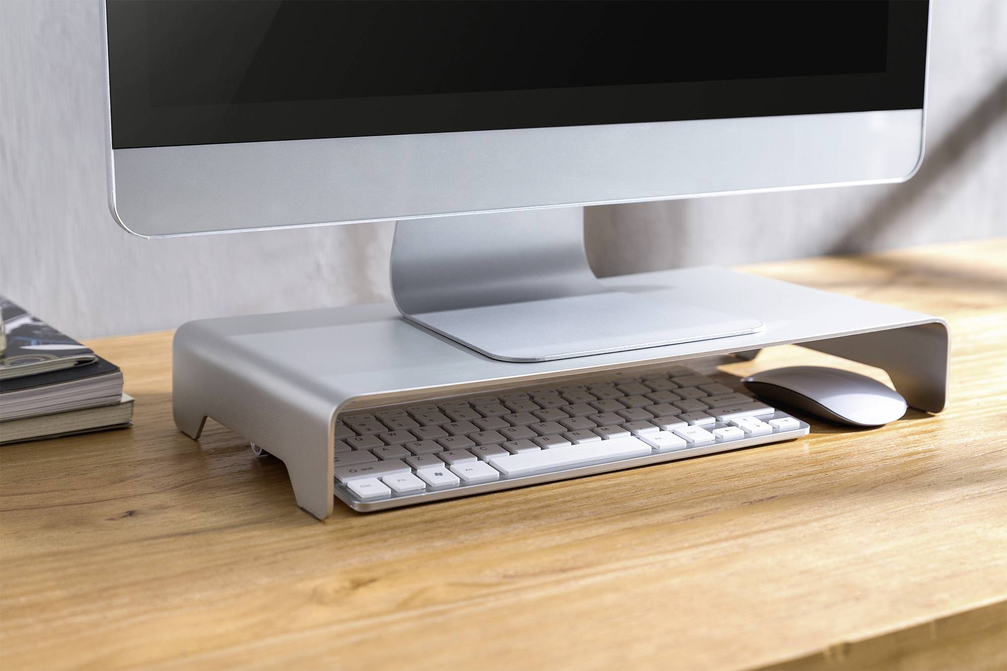 Ein Computermonitor steht auf einem grauen Ständer auf einem Holztisch. Darunter sind eine Tastatur und eine Maus platziert.