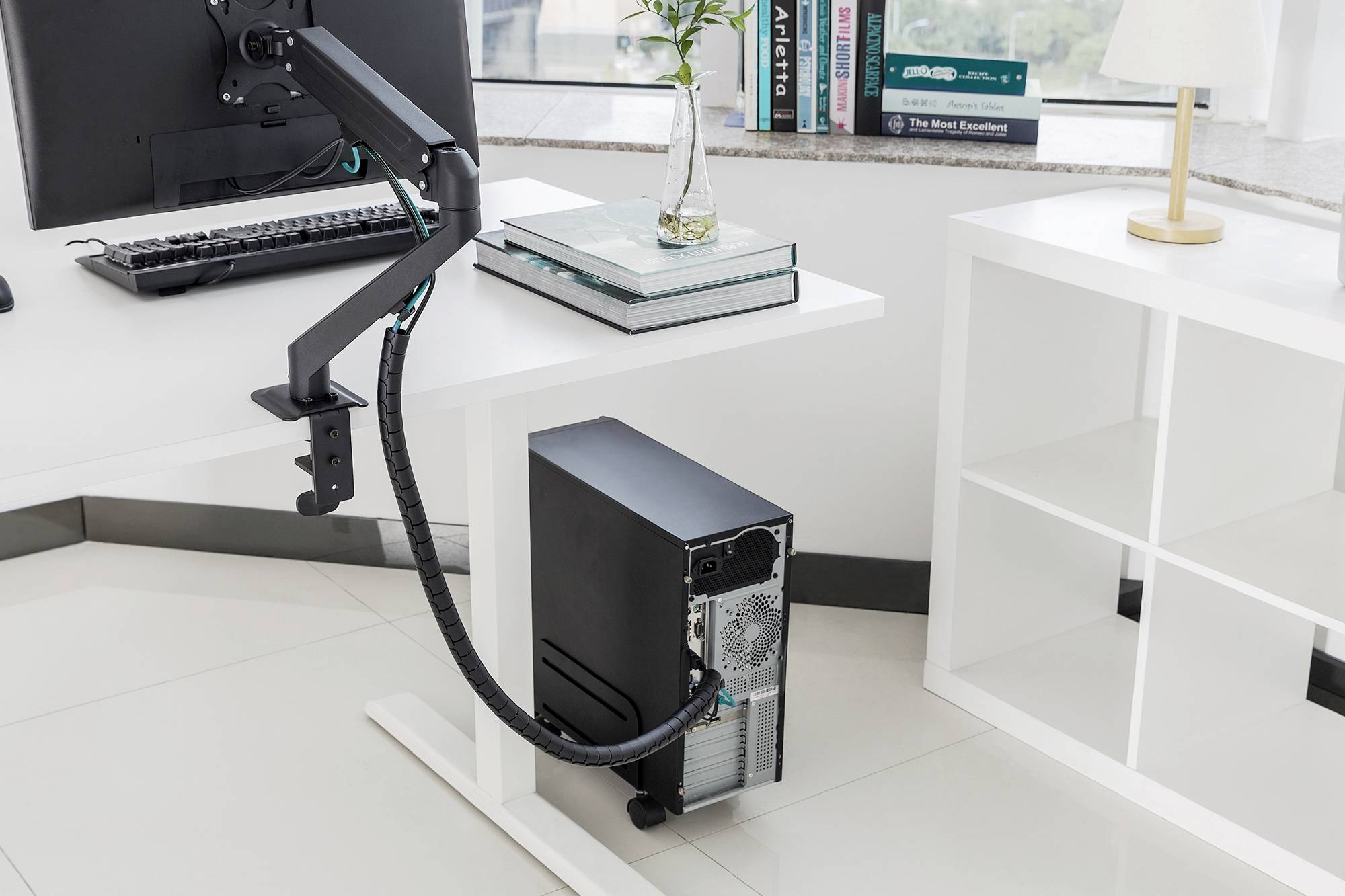 Ein Computer mit einem Kabelmanagementsystem steht auf einem Schreibtisch in einem modernen Büro. Bücher und Lampe im Hintergrund.