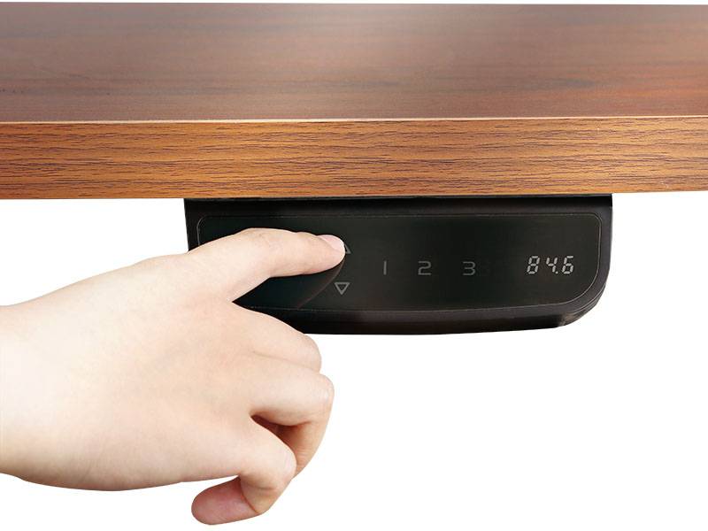 Eine Hand drückt einen Knopf an einem Bedienfeld unter einem Holztisch, das Höhenverstellungszahlen anzeigt.