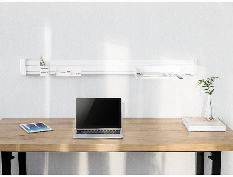 Ein aufgeräumter Schreibtisch mit einem Laptop, einem Tablet, einem Buch und einer Pflanze. An der Wand eine weiße Regalhalterung mit Stiften.