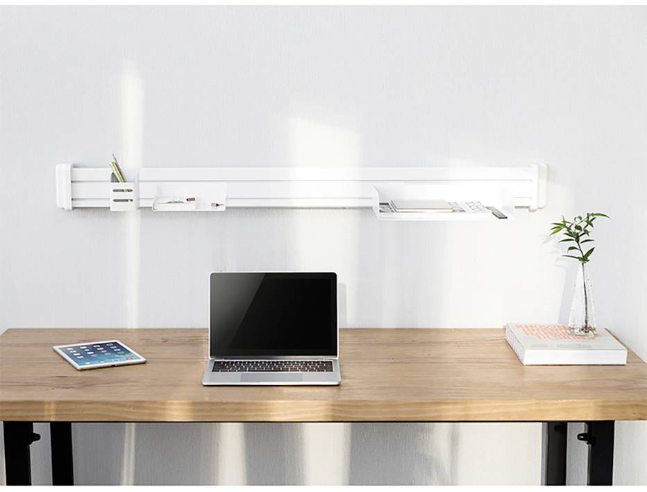 Ein minimalistischer Schreibtisch mit einem Laptop in der Mitte, einem Tablet links und einem Buch mit einer Pflanze rechts. Eine weiße Regalablage ist an der Wand montiert.
