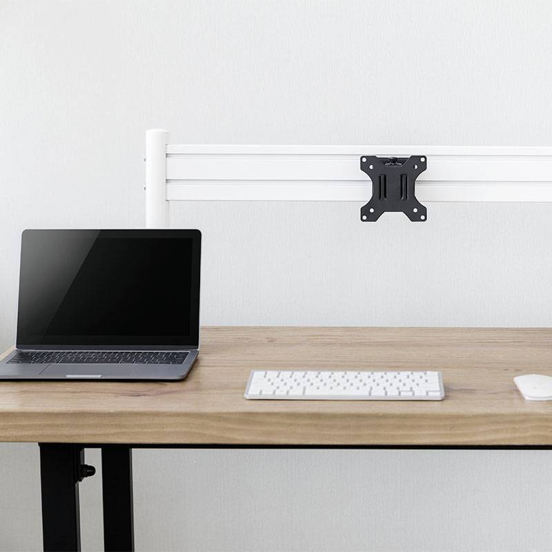 Ein Laptop, eine Tastatur und eine Maus auf einem Schreibtisch. An der Wand eine Monitorhalterung ohne Bildschirm.