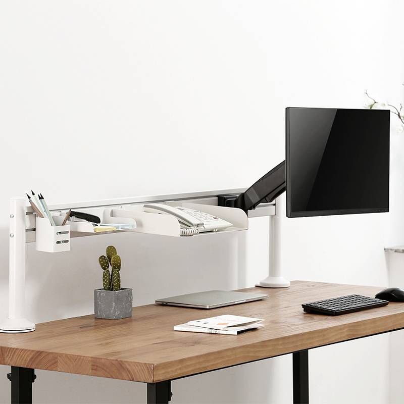 Ein moderner Schreibtisch mit Holzoberfläche zeigt einen Monitor auf einem Ständer, eine Tastatur, eine Maus und Pflanzen im Hintergrund.