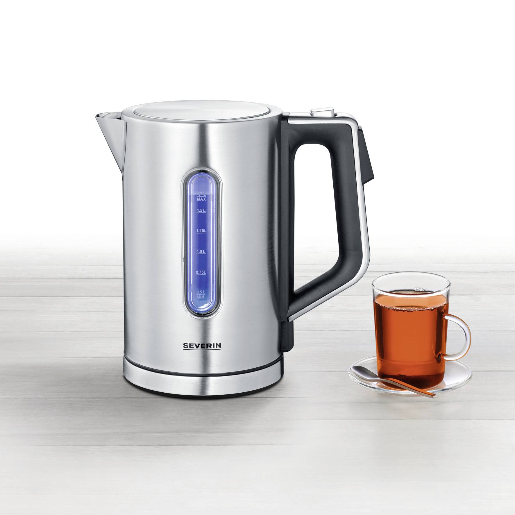 Ein Edelstahlwasserkocher mit Wasserstandsanzeige neben einer Tasse Tee; beide auf einer hellen, glatten Oberfläche.