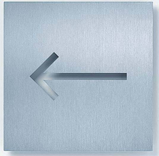 Ein Metallschild mit einem ausgeschnittenen Pfeil nach links, das als Wegweiser oder Hinweis auf eine Richtung dient.