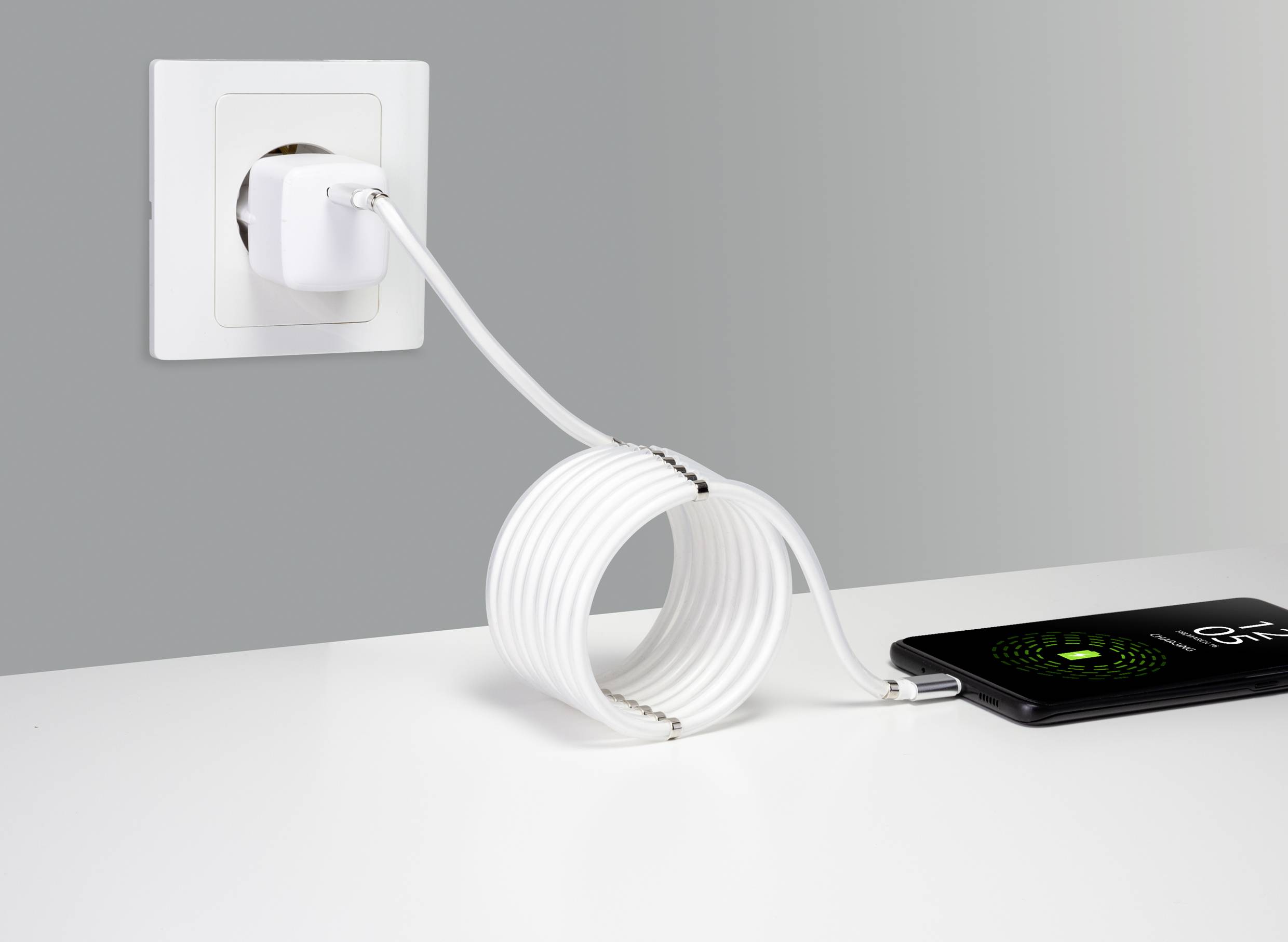 Ein Smartphone wird mit einem langen weißen USB-Kabel an einem Ladegerät in einer Steckdose aufgeladen und zeigt einen Ladebildschirm.