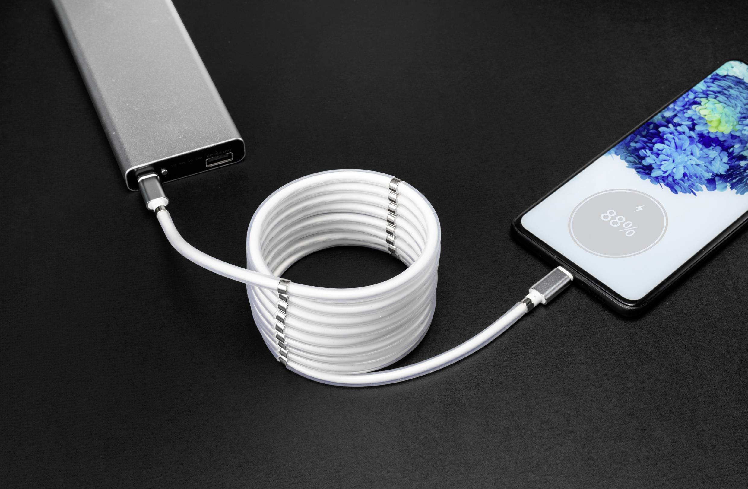 Ein Smartphone wird mit einem weißen Kabel von einer Powerbank geladen. Auf dem Bildschirm des Smartphones ist der Ladezustand '88%' sichtbar.