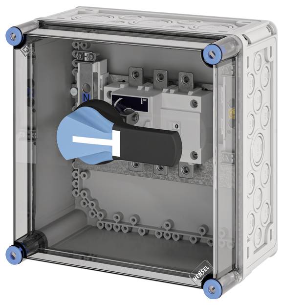 Ein transparenter Kasten mit einem großen blauen Schalter vorne, montiert auf einer grauen Platte mit elektrischen Anschlüssen innen.