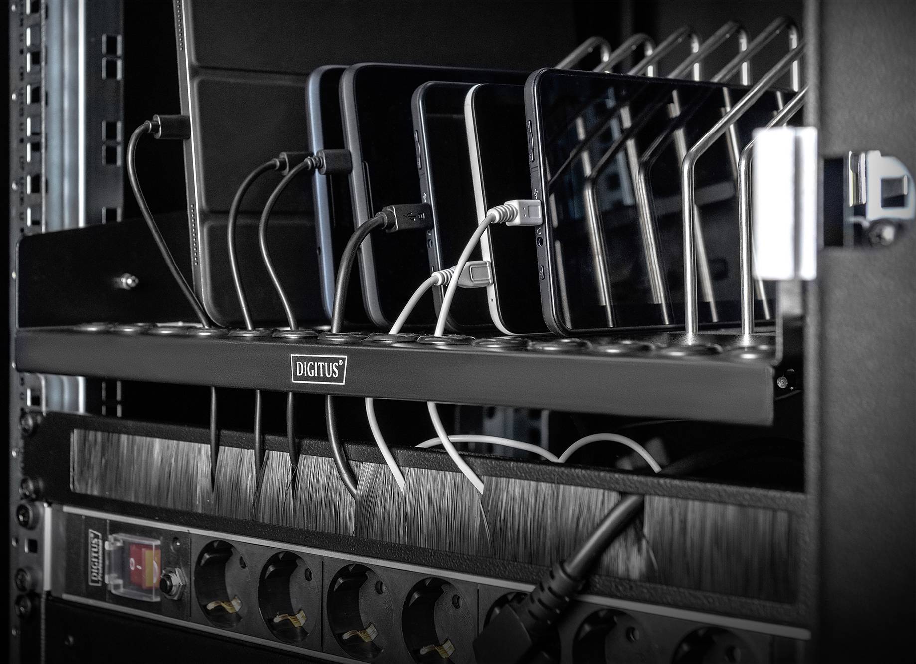 Mobiltelefone werden in einer Ladestation mit mehreren USB-Kabeln aufgeladen. Die Station befindet sich in einem IT-Rack.