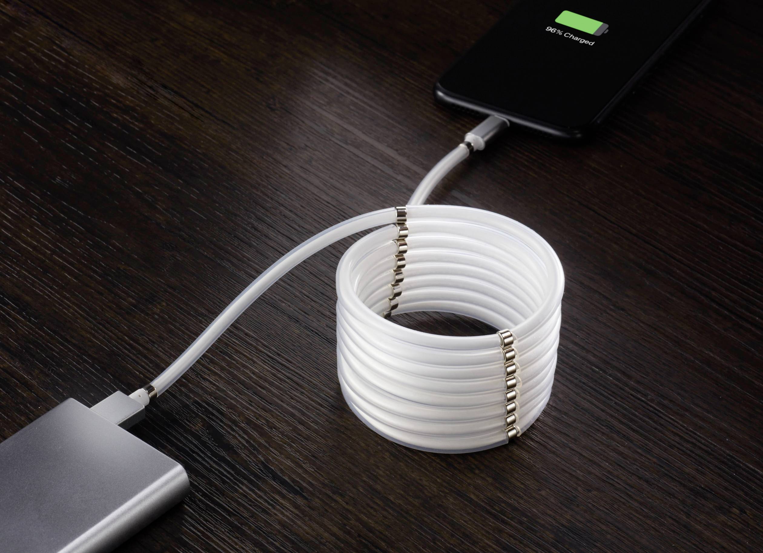 Ein Smartphone wird mit einem aufgerollten USB-Kabel von einer Powerbank geladen. Das Telefon zeigt '100% geladen' an.