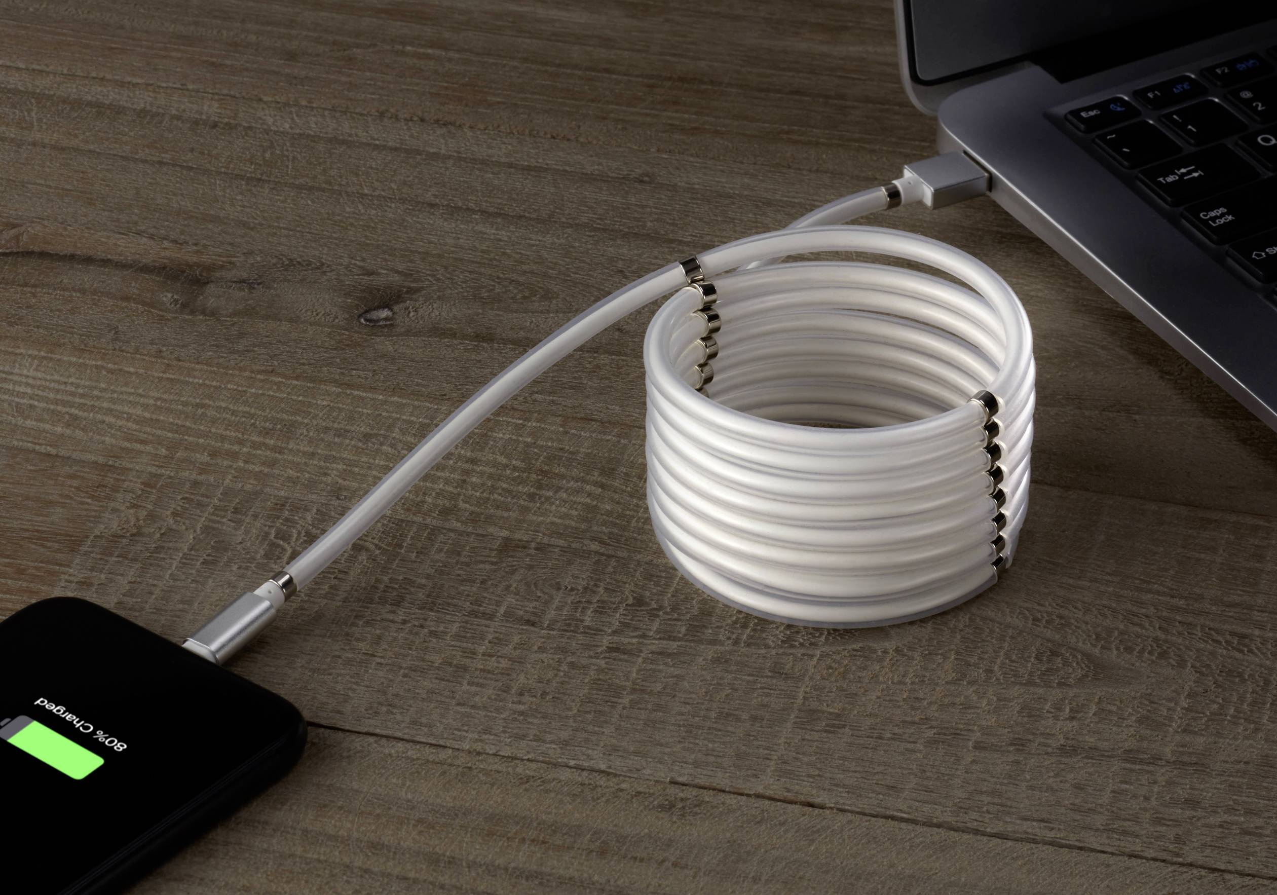 Ein Laptop wird über ein USB-Kabel mit einem weißen, aufgerollten Spiralkabel an einer Powerbank auf einem Holztisch aufgeladen.