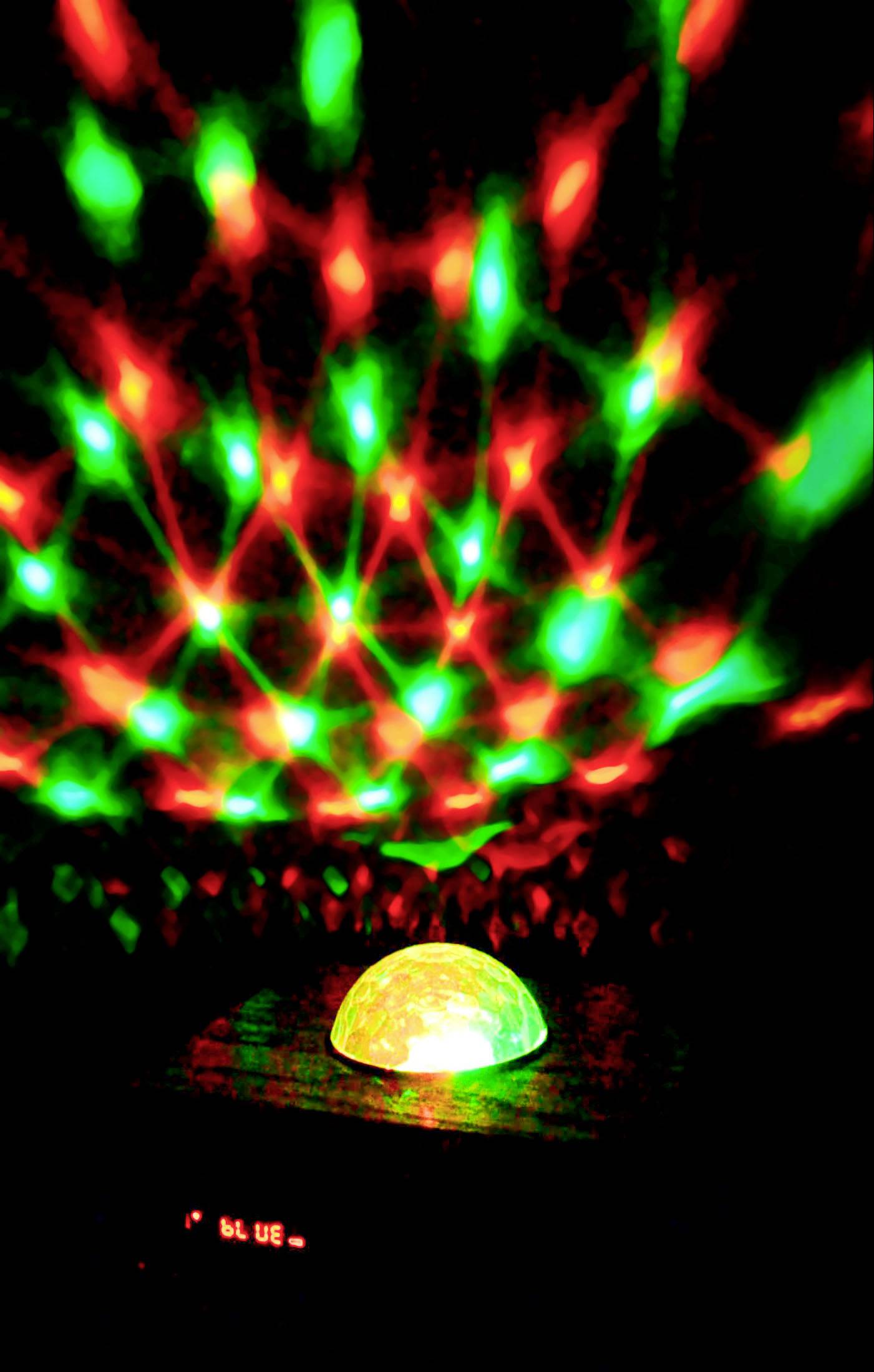 Ein Leuchtgerät projiziert grüne und rote Lichteffekte an die Decke, die Muster wie Sterne oder Blumen bilden.