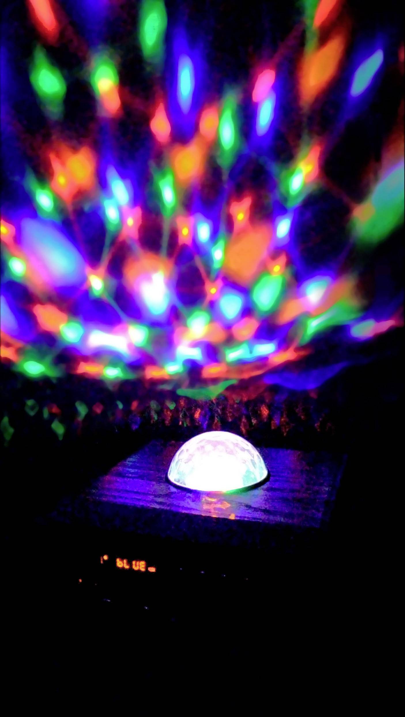 Ein leuchtendes, buntes Lichtobjekt projiziert farbige Muster an eine dunkle Wand, erzeugt eine stimmungsvolle Atmosphäre.