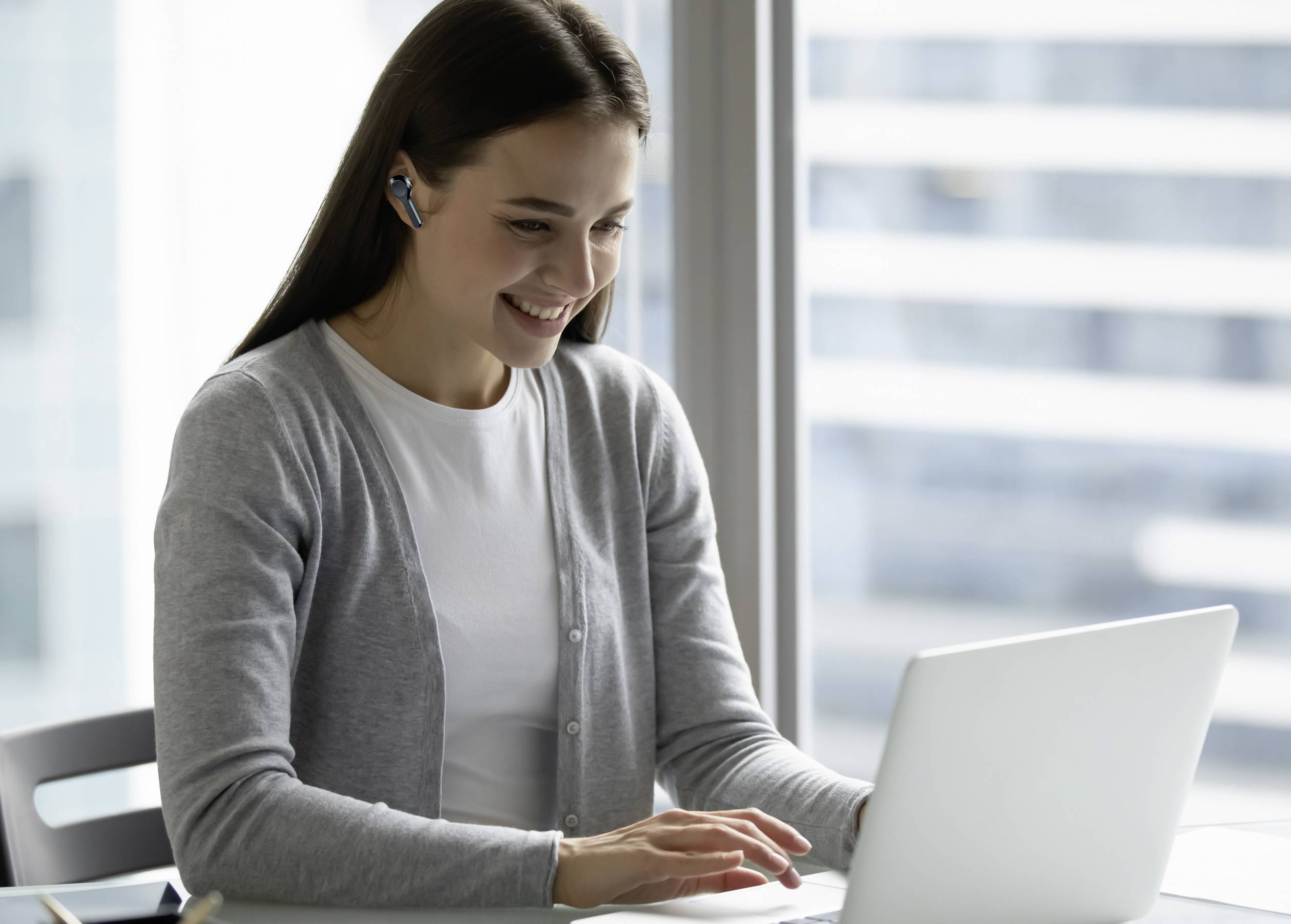 Eine lächelnde Frau mit Headset sitzt vor einem Laptop in einem modernen Büro, vertieft in ihre Arbeit.