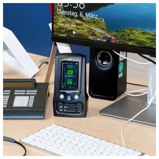 Desktop-Schreibtisch-Setup mit Monitor, Lautsprecher, Tastatur und einem zentralen Gerät mit grünem digitalen Display mit den Zahlen 29 und 58.