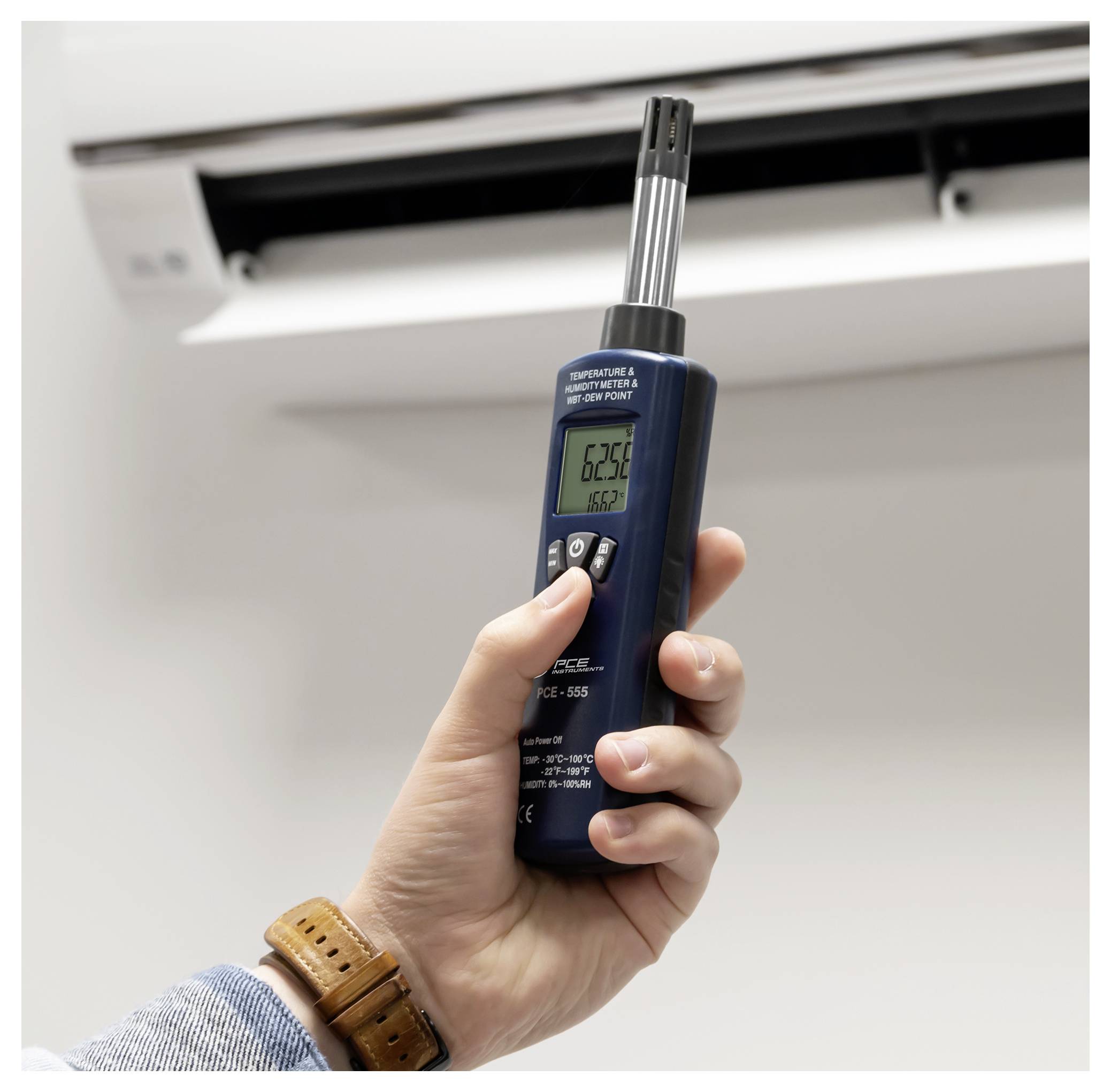 Hand hält ein digitales Thermometer in der Nähe einer Klimaanlage-Lüftung und misst die Innentemperatur.