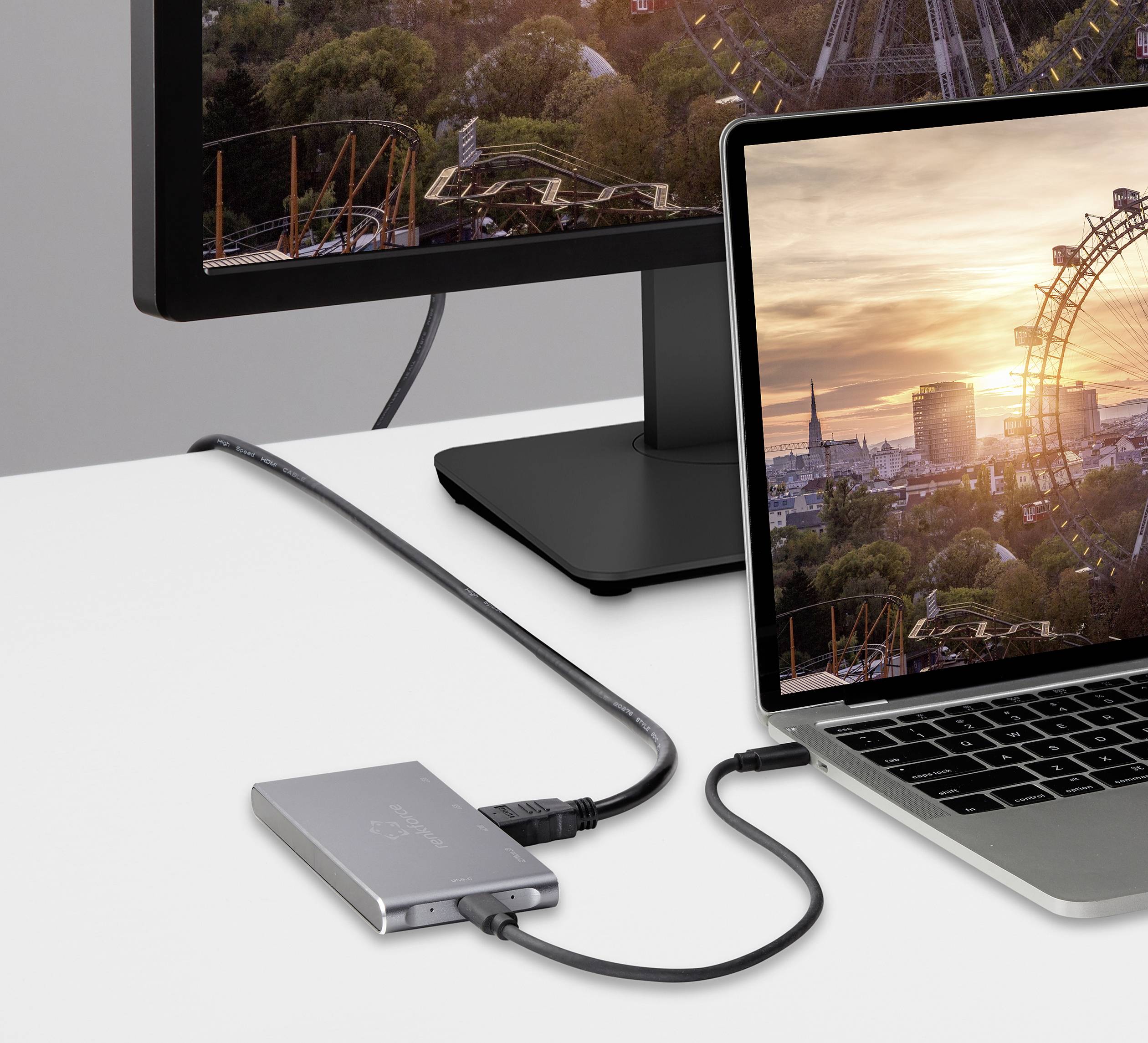 Ein Laptop sitzt auf einem Tisch, verbunden mit einem Monitor. Auf beiden Bildschirmen ist ein Riesenrad und eine Stadt bei Sonnenuntergang zu sehen.