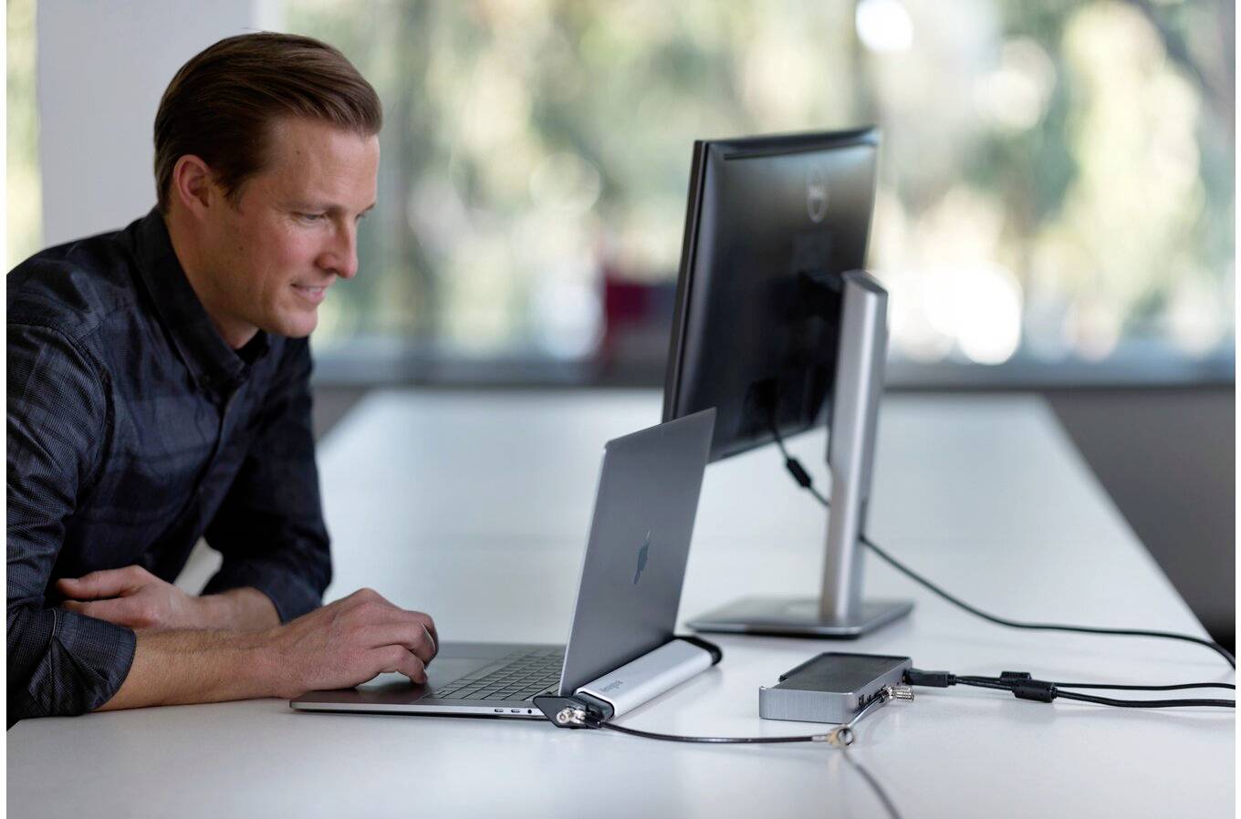 Eine Person arbeitet an einem Laptop, der an einen Monitor angeschlossen ist, auf einem Tisch in einem Büro.