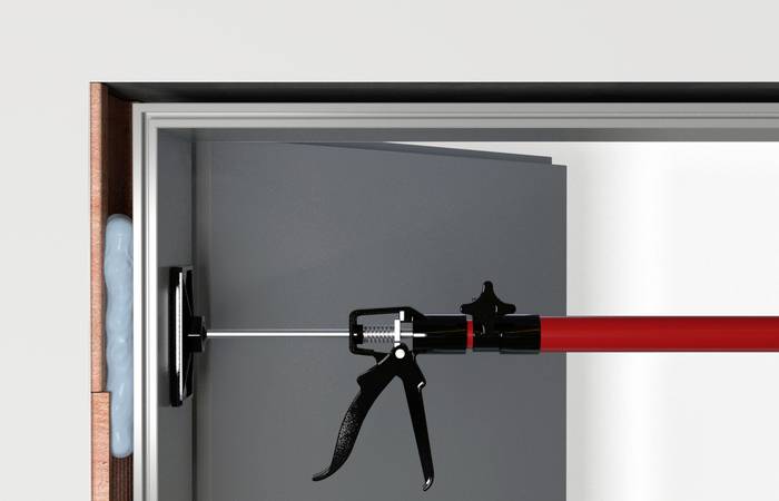 Ein rotes Werkzeug wird verwendet, um eine Tür mit Schaum an den Rändern zu sichern. Es drückt gegen die Tür, während sie geschlossen wird.