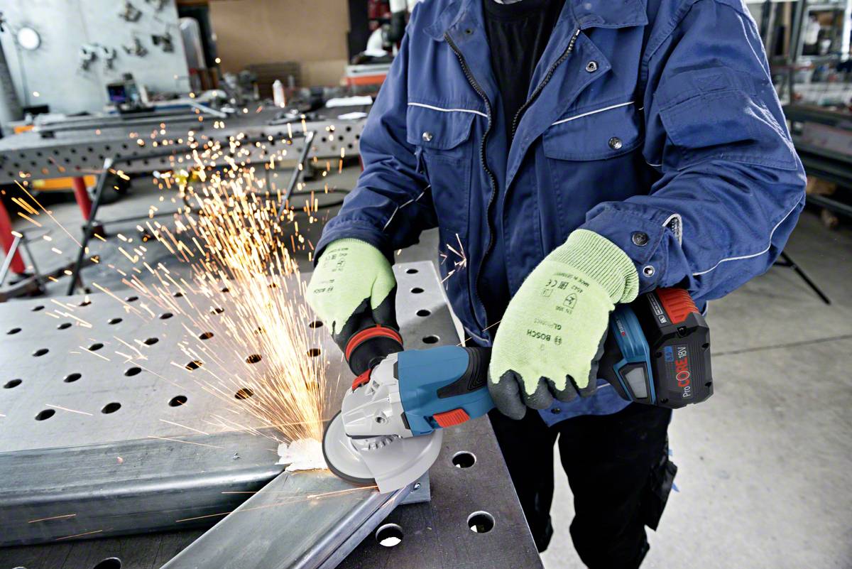Eine Person schleift Metall mit einem Winkelschleifer, Funken fliegen. Die Arbeitsumgebung wirkt industriell, mit Metalltisch und Maschinen.
