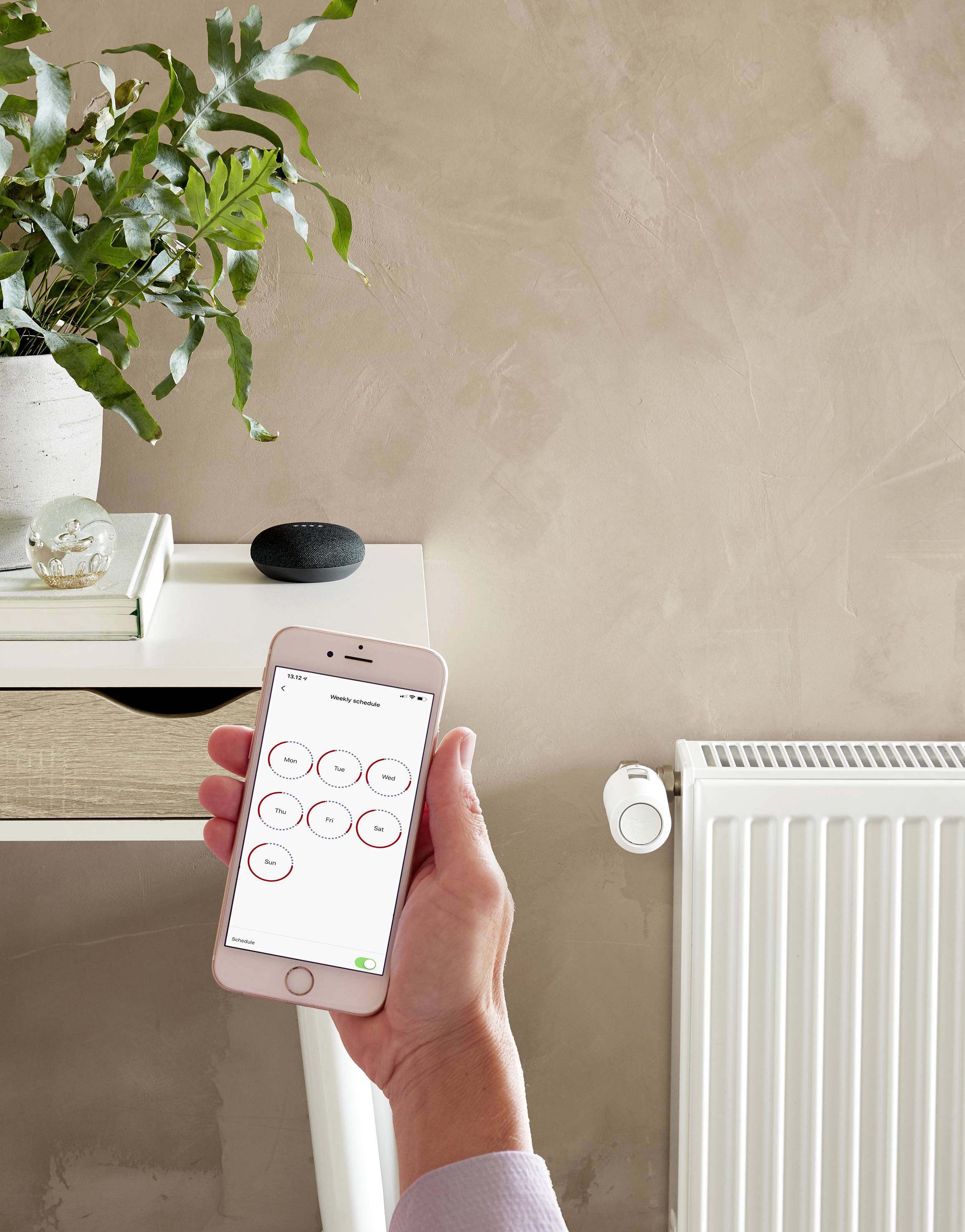 Eine Person steuert mit einem Smartphone die Heizkörpertemperatur in einem modernen Raum. Ein Tisch und eine Pflanze sind im Hintergrund.