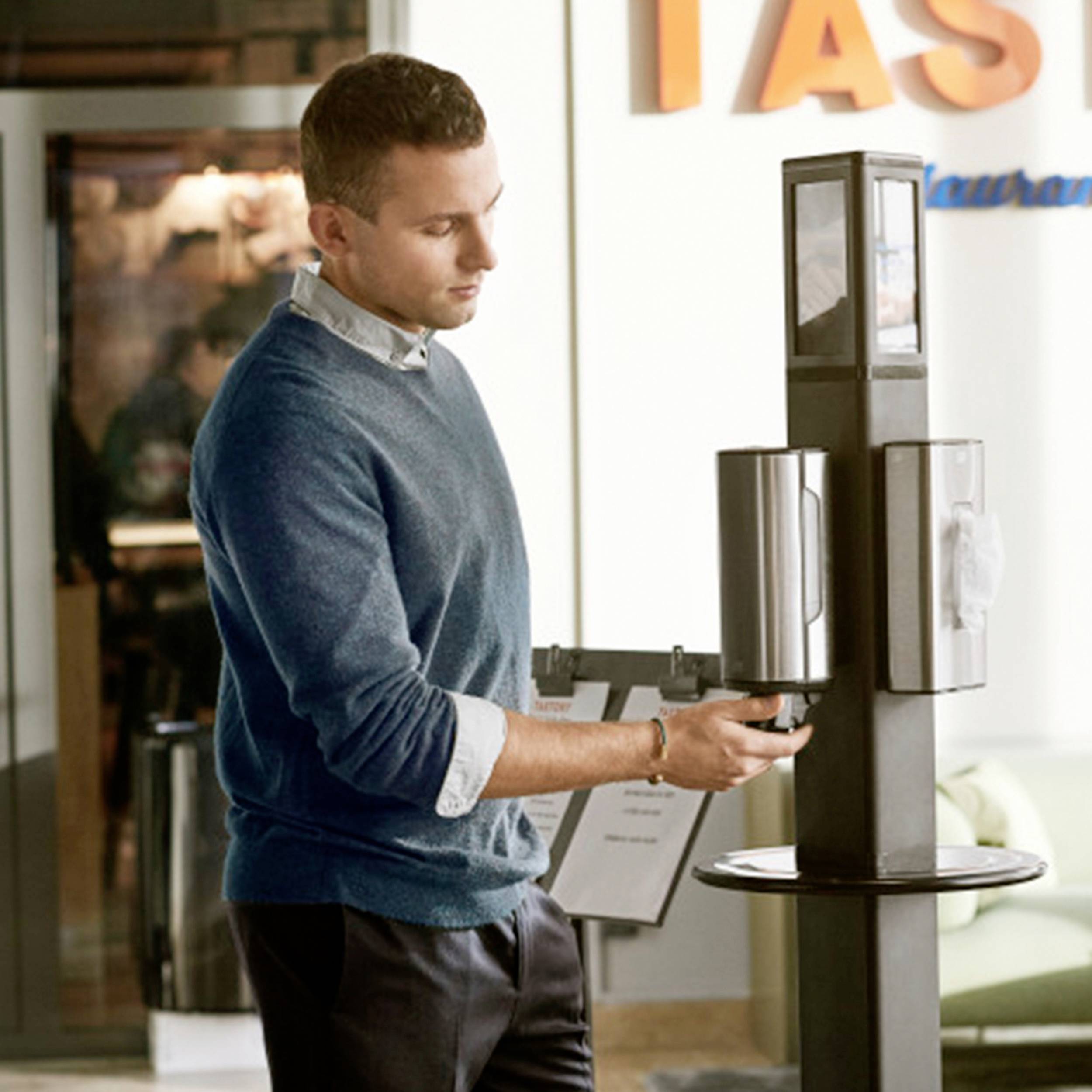 Eine Person steht in einem modernen Restaurant und benutzt einen berührungslosen Händedesinfektionsspender.