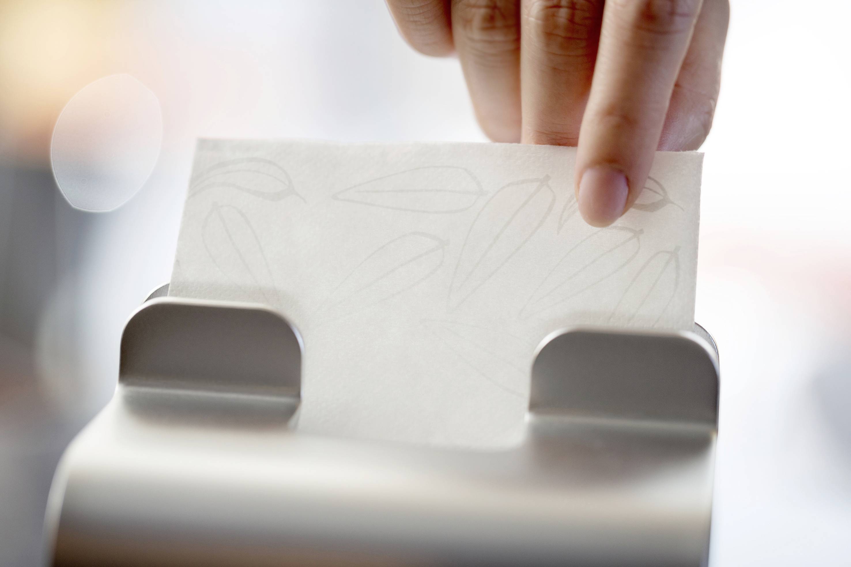Hand entnimmt Papierhandtuch aus einem Spender.