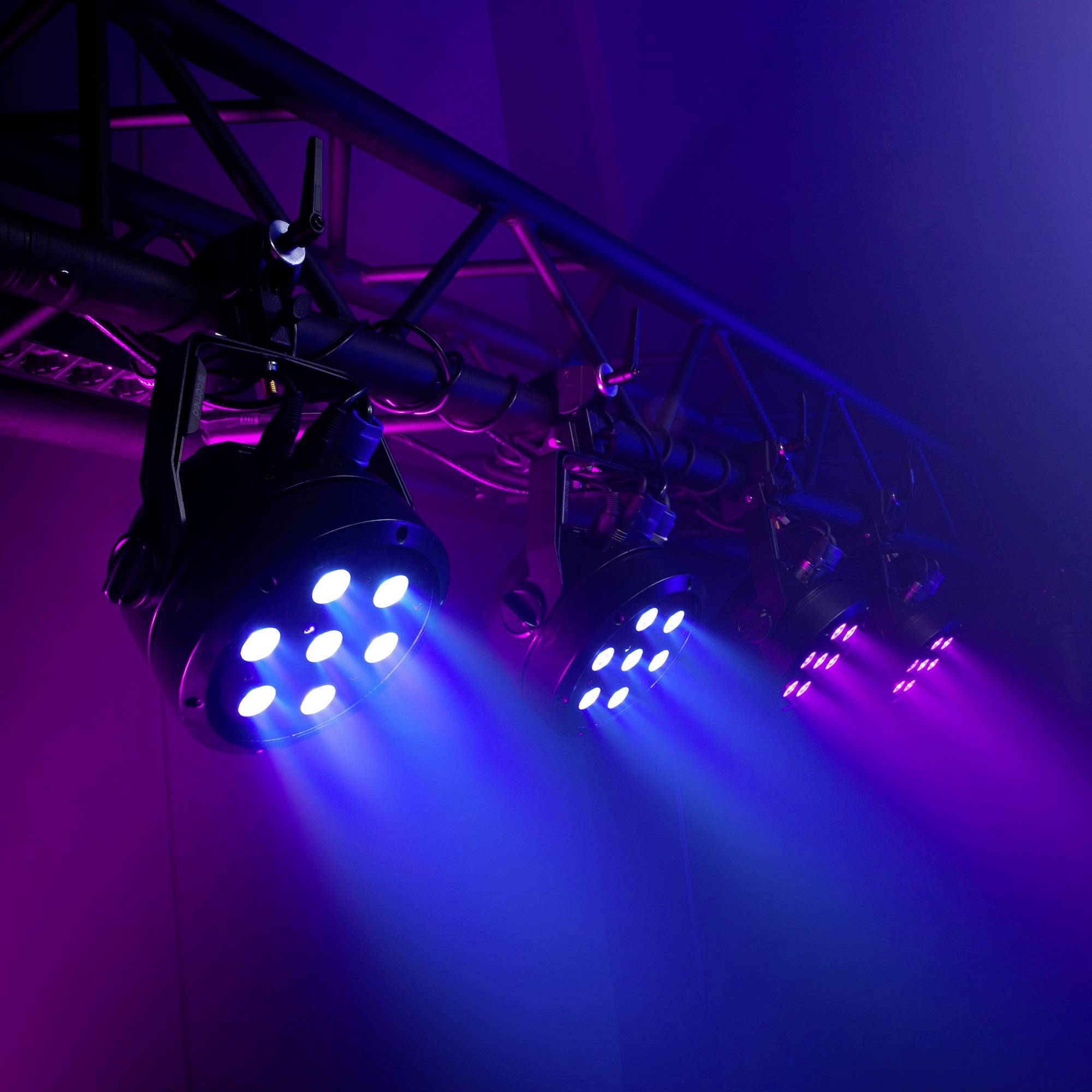 Mehrere Bühnenscheinwerfer strahlen blaues und violettes Licht aus, das auf einer Veranstaltung oder in einem Theater eine stimmungsvolle Atmosphäre schafft.