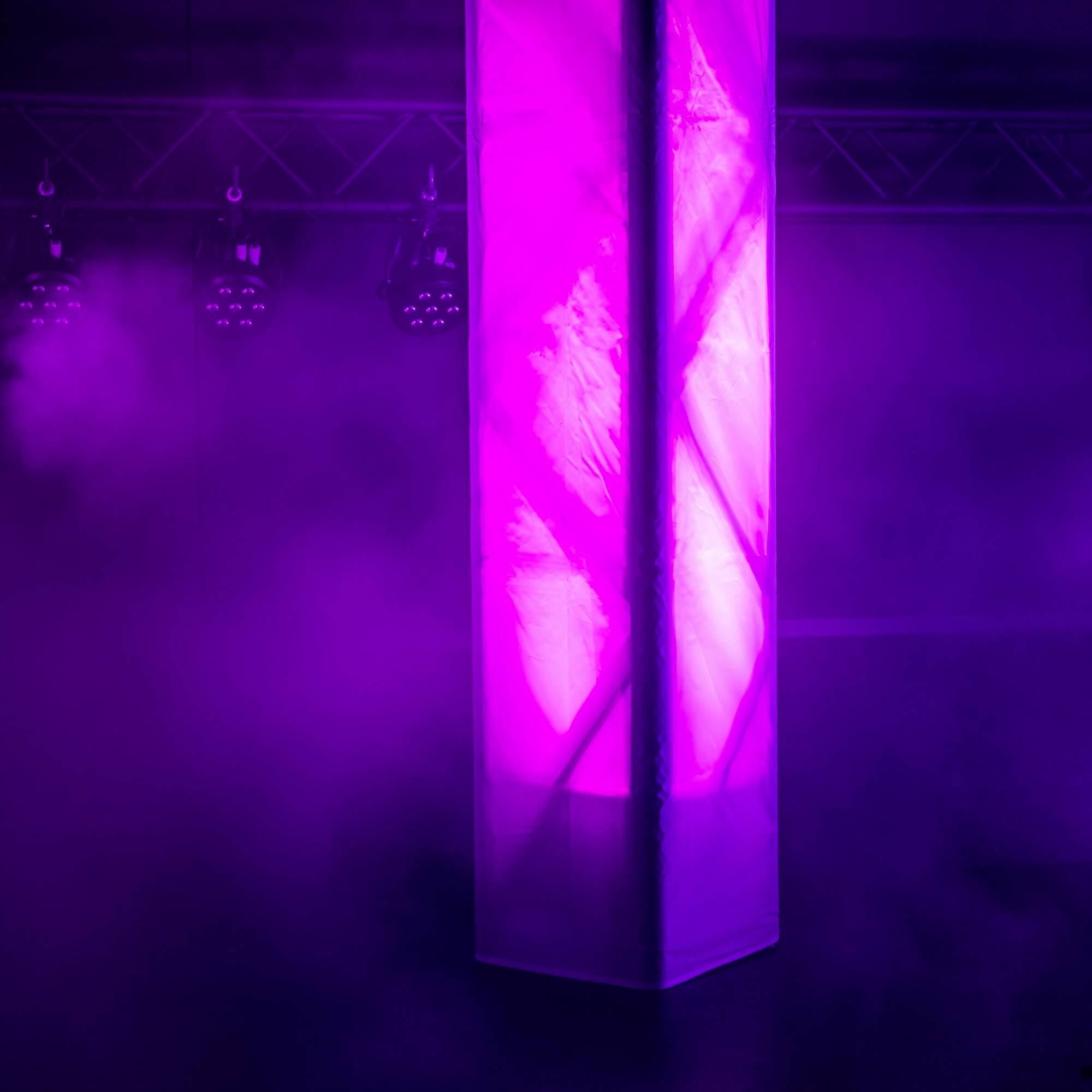 Eine leuchtende Säule erstrahlt in violettem Licht auf einer Bühne, umgeben von Bühnenlichtern und sanftem Nebel.