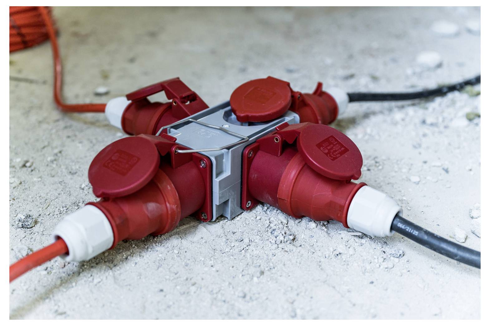 Roter industrieller elektrischer Stromverteiler mit vier angeschlossenen Kabeln auf einem Betonboden.