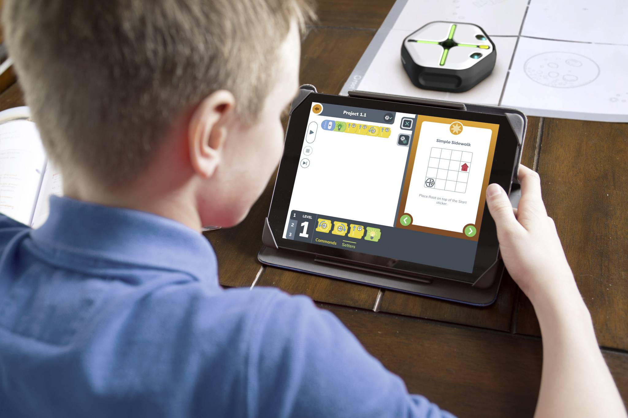 Ein Kind hält ein Tablet, auf dem eine Lern-App mit einem Koordinatensystem angezeigt wird. Ein kleiner Roboter liegt auf dem Tisch.