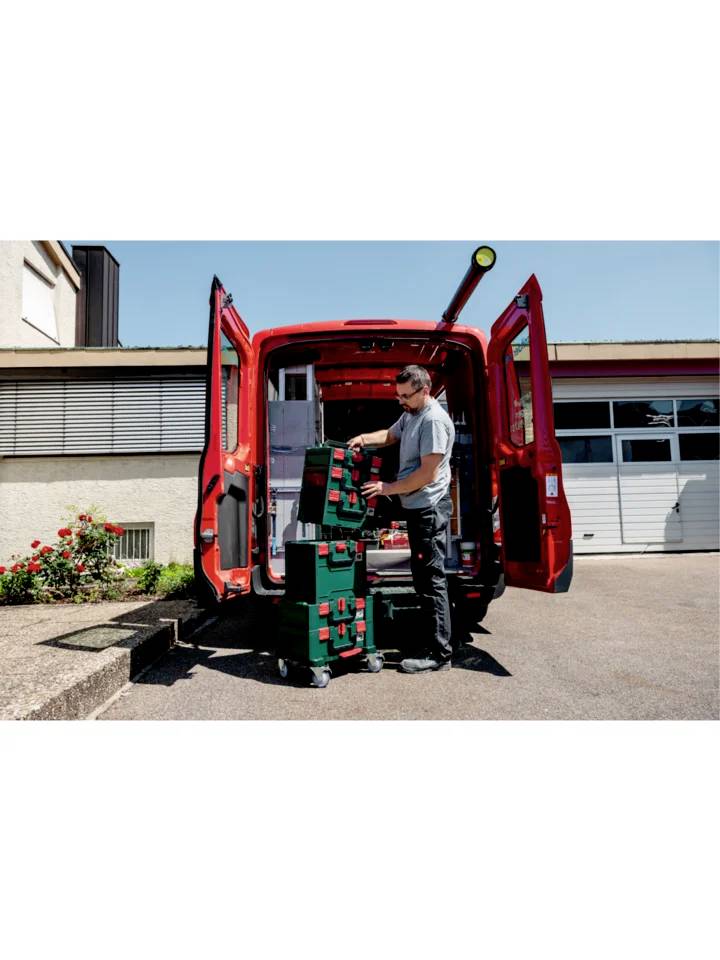 Ein Mann entlädt Werkzeugkoffer aus einem roten Lieferwagen auf einem Industriegelände.