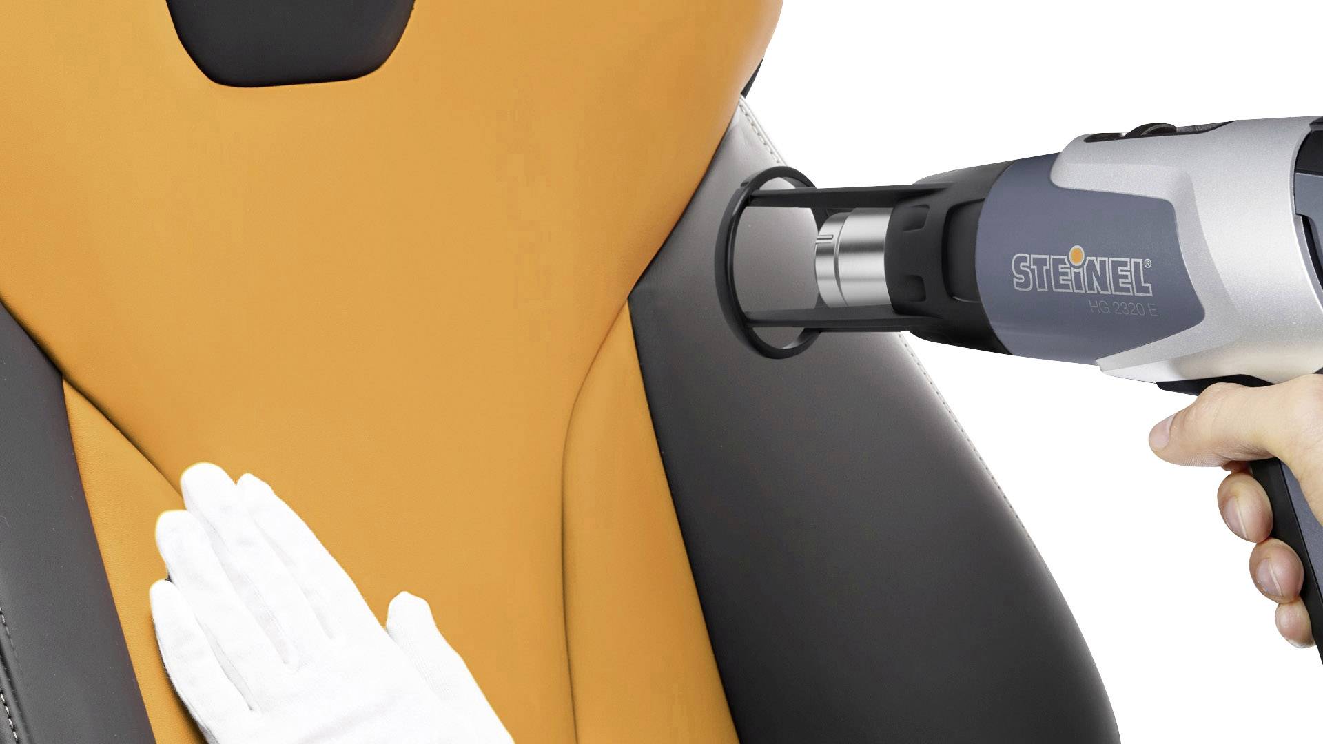 Eine Person bearbeitet einen orange-schwarzen Autositz mit einem Heißluftföhn. In der anderen Hand trägt sie einen weißen Handschuh.