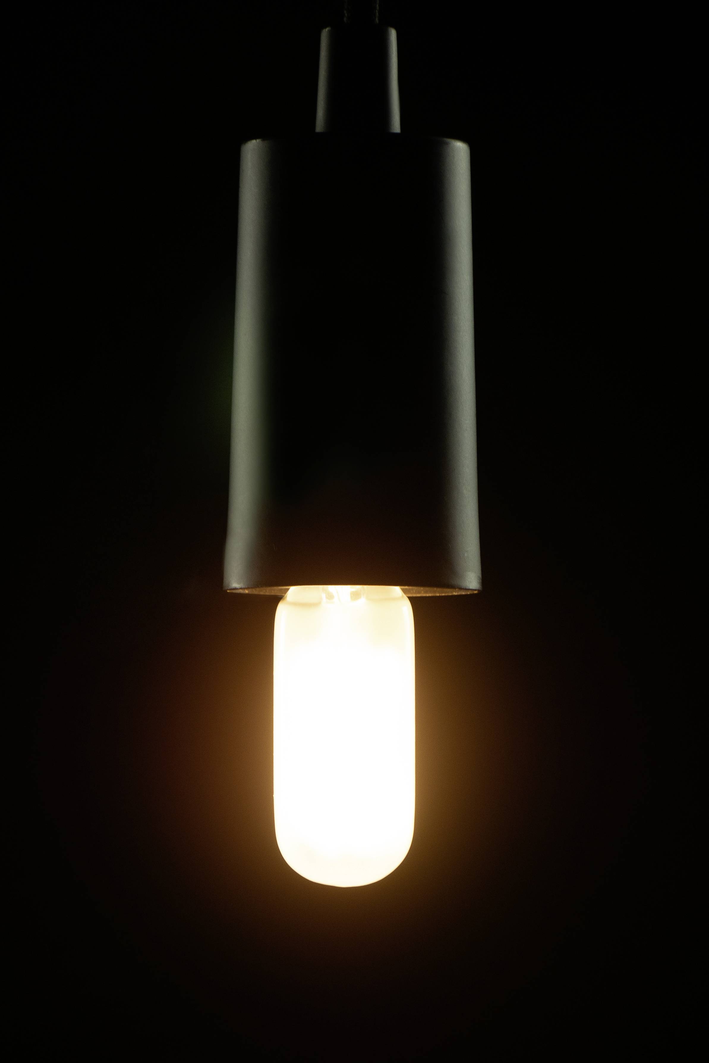 Eine einzelne, hängende Glühbirne leuchtet in der Dunkelheit.