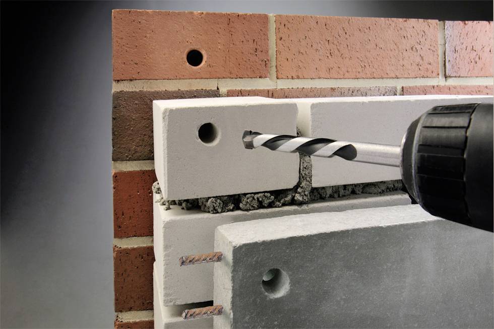 Ein Bohrer durchstößt eine Backsteinwand, um eine Öffnung in einem Hohlziegel zu schaffen.