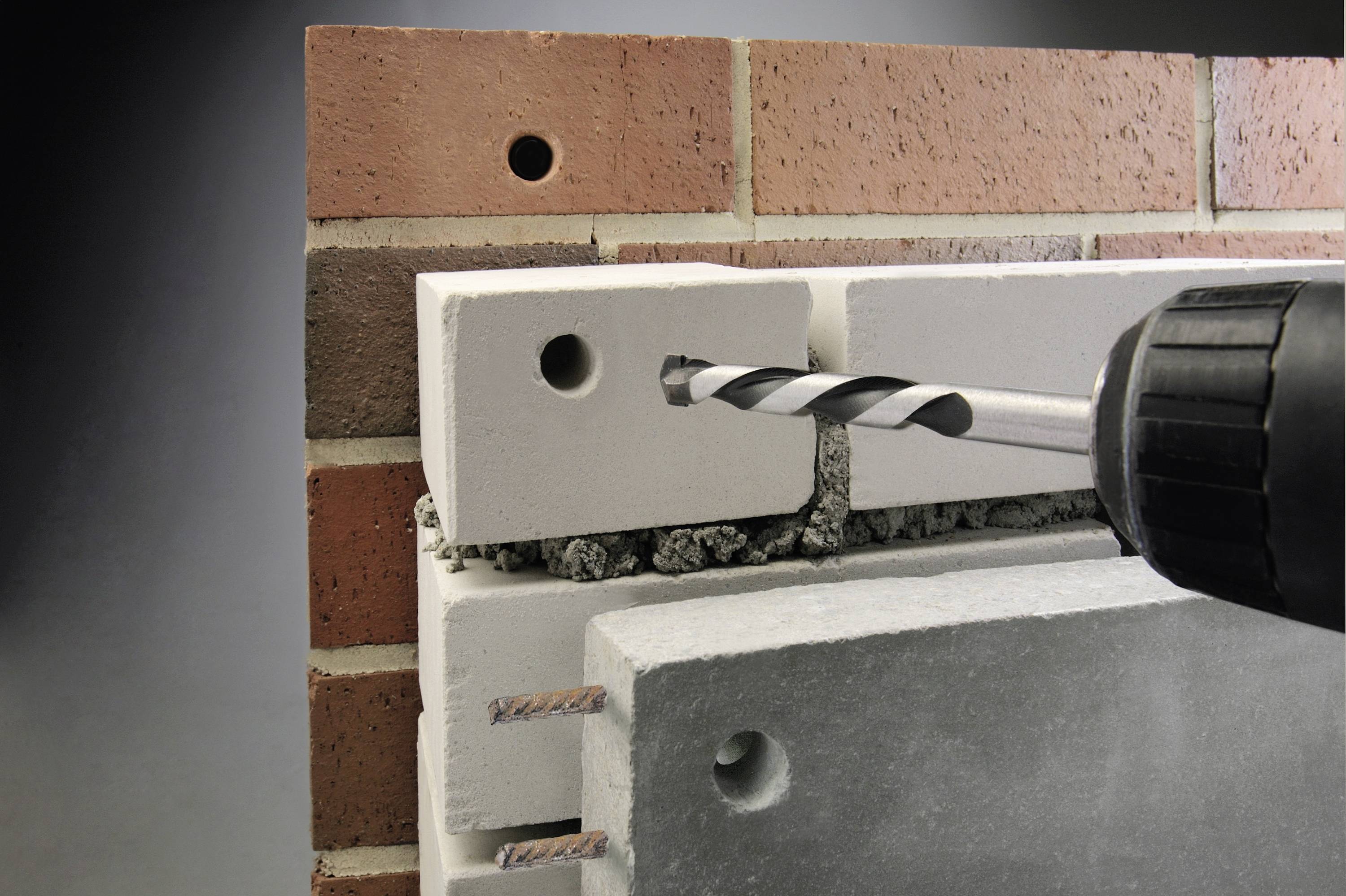 Bohrmaschine mit Bohrer im Einsatz durch eine Mauer aus weißen Kalksandsteinen, zeigt die Methode zur Wandbefestigung.