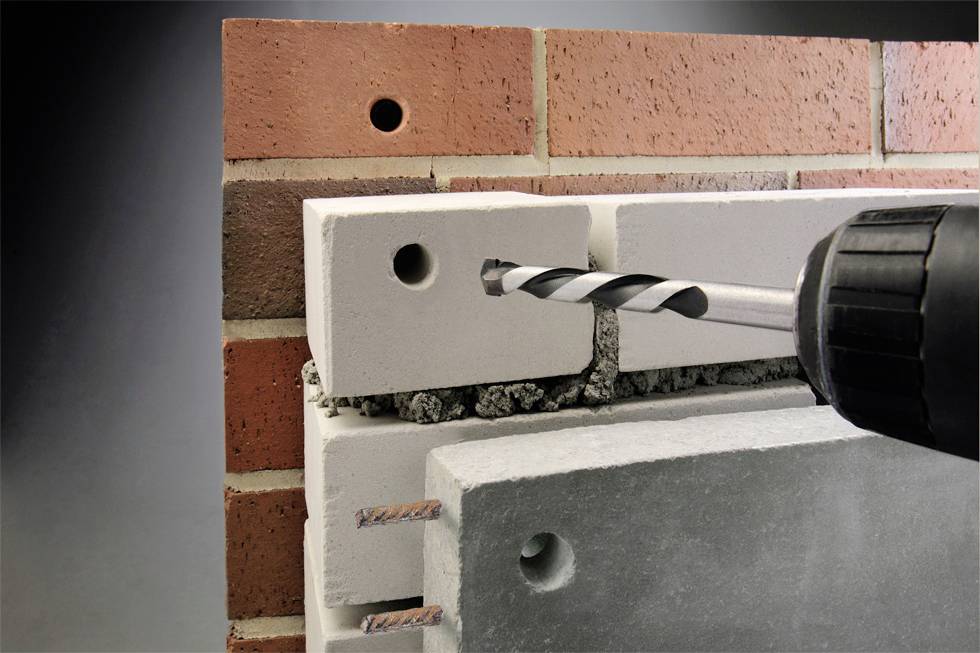 Ein Bohrer wird in eine Betonplatte mit Klinkerfassade eingeführt, um ein Loch zu bohren. Die Szene zeigt den Bohrvorgang im Detail.