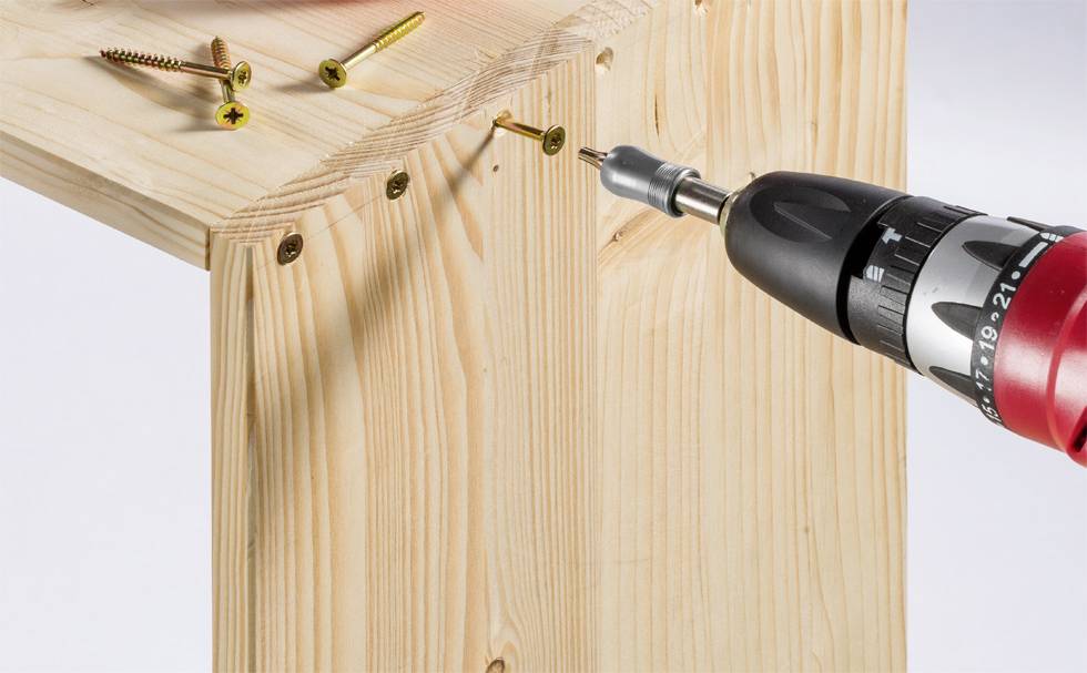 Ein Akkuschrauber zieht eine Schraube in ein Holzbrett. Mehrere Schrauben liegen lose auf dem Brett.