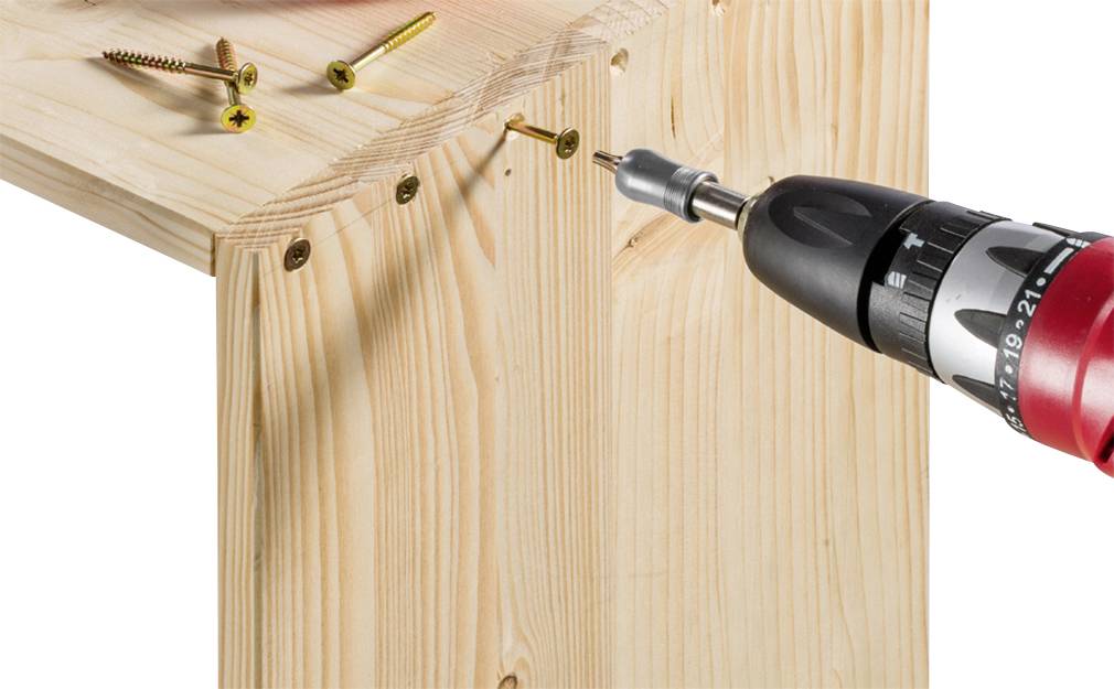 Ein Akkuschrauber zieht eine Schraube in ein hölzernes Brett ein. Mehrere Schrauben sind bereits in das Holz geschraubt.