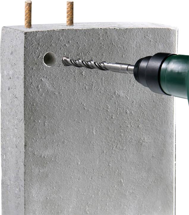 Eine Bohrmaschine bohrt ein Loch in einen Betonblock. Oben sind zwei Bewehrungsstäbe zu sehen.