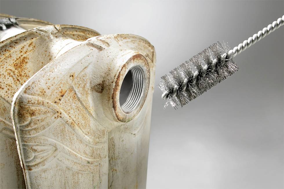 Ein verrosteter Metallkanister wird mit einer Metallbürste gereinigt. Die Bürste ist nahe der Öffnung des Kanisters positioniert.