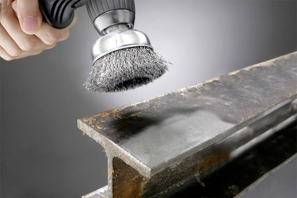 Nahaufnahme einer Hand, die eine Drahtbürste an einem Winkelschleifer hält und Rost von einem Metallträger entfernt.