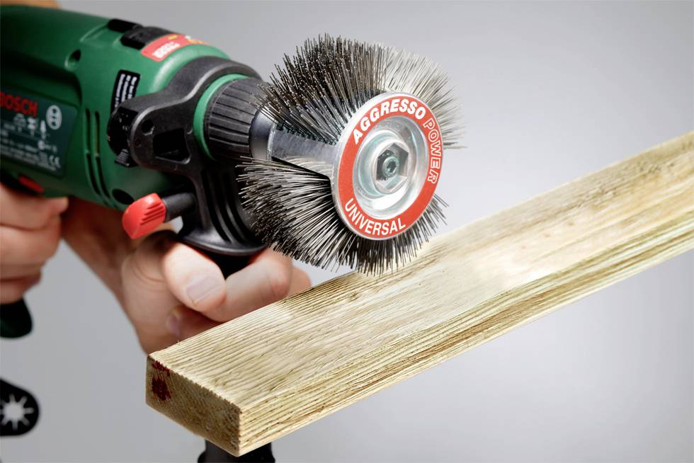 Eine Person schleift mit einer elektrischen Schleifbürste ein Stück Holz ab. Die Schleifbürste hat die Aufschrift 'Aggresso Power Universal'.