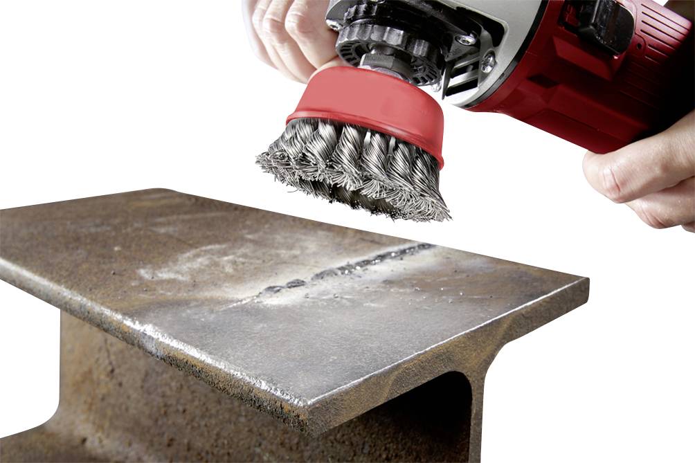 Eine Hand hält eine rot-schwarze Drahtbürste, die an einem Winkelschleifer befestigt ist, um Rost von einem Metallträger zu entfernen.