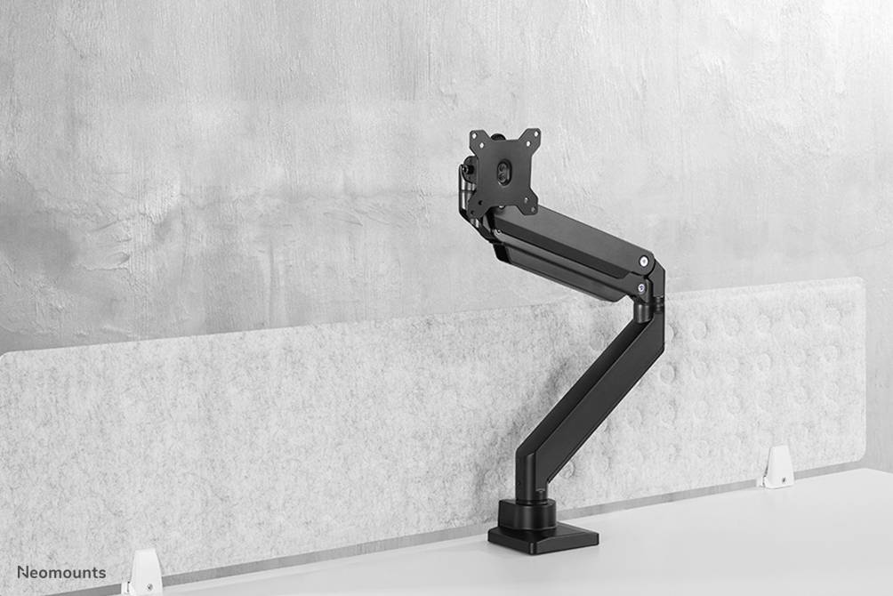 Ein Monitorarm aus schwarzem Metall ist auf einem weißen Tisch montiert, vor einer grauen Wand.