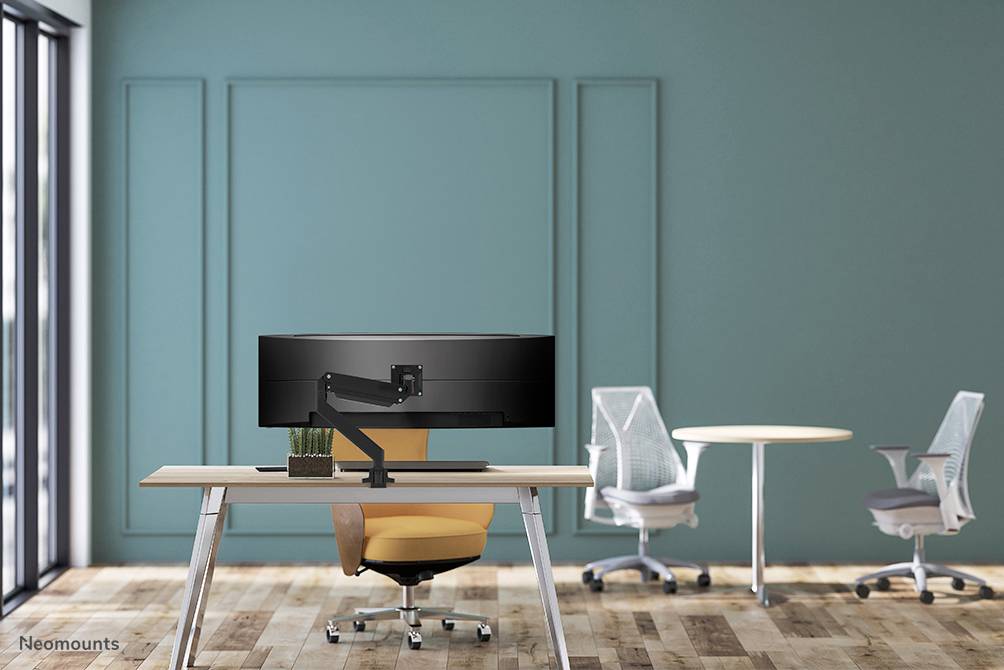 Moderner Bürostuhl und Schreibtisch mit einem großen Bildschirm in einem stilvollen, minimalistischen Raum mit grünem Wandhintergrund.