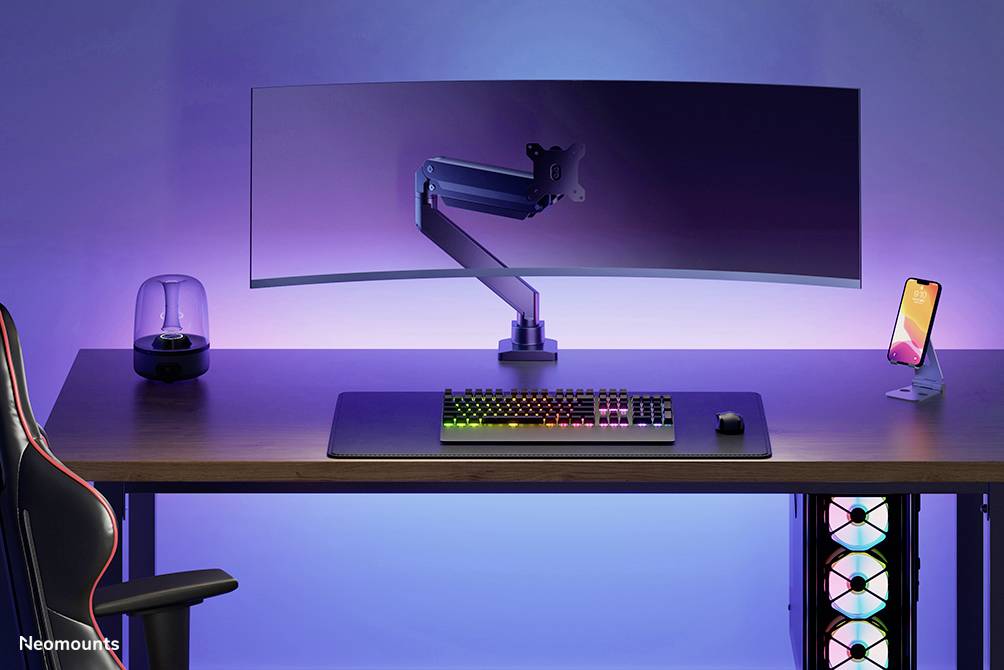 Ein moderner Schreibtisch mit einem gebogenen Monitor, beleuchteter Tastatur, Maus, Handyhalterung, Lautsprecher und beleuchtetem Computergehäuse.