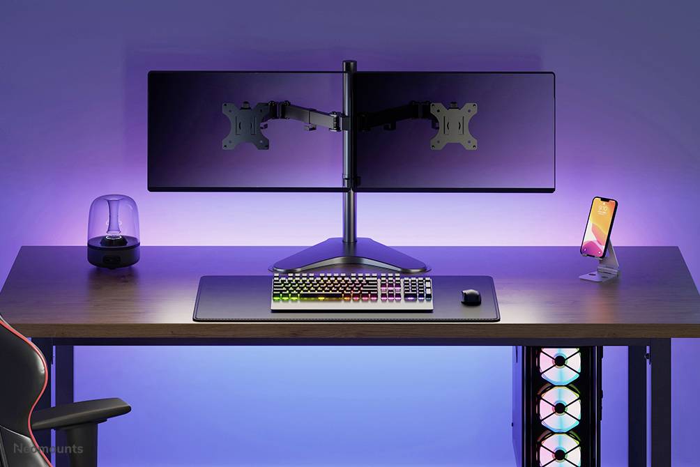 Ein Schreibtisch mit RGB-Tastatur, Maus, zwei Monitorhalterungen ohne Monitore, Smartphone-Halterung und beleuchteten Lüftern, umgeben von sanfter Beleuchtung.