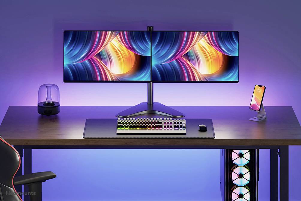 Ein moderner Schreibtisch mit dualen Monitoren zeigt bunte Abstraktionen. Ein beleuchtetes Keyboard und Maus sind zentral platziert.