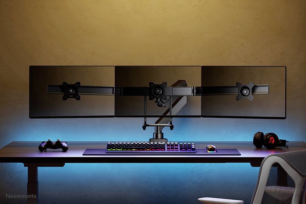 Ein Schreibtisch mit drei Monitoren auf einem Ständer, einer RGB-Tastatur, einer Maus, einem Controller und einem Headset.